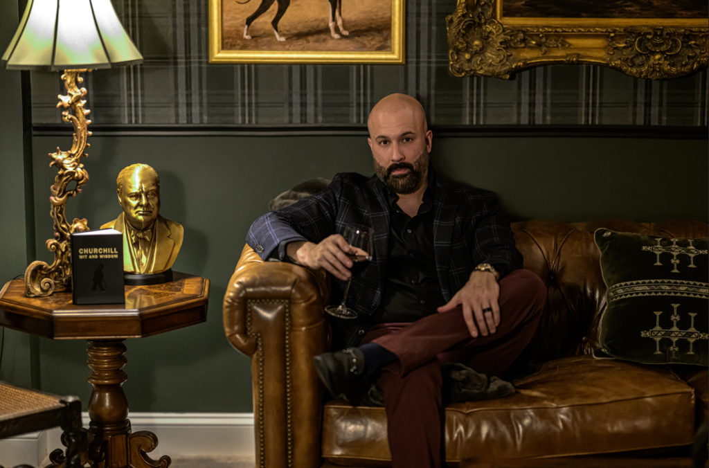 Chaudry Ghafoor, founder of The Masculine Home, seated in a traditional study with leather sofa, artwork, and Churchill bust.